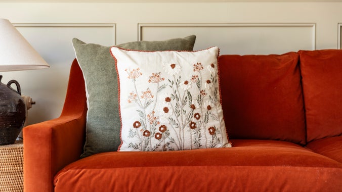 A cream cushion with burnt orange and sage green embroidered floral accents from the 2025 autumn/winter collection